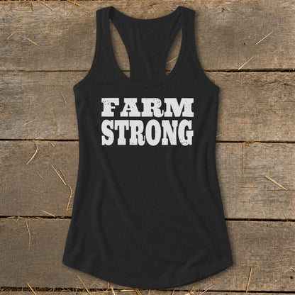 Black women's racerback tank top featuring white distressed text that reads "FARM STRONG" on a rustic wooden background.