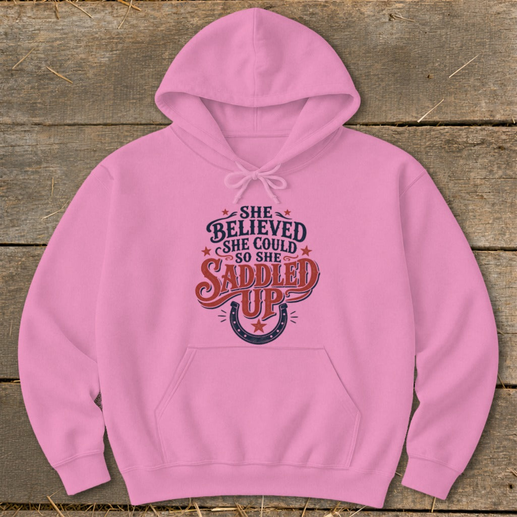 Pink hoodie with "She believed she could so she saddled up" graphic and horseshoe.