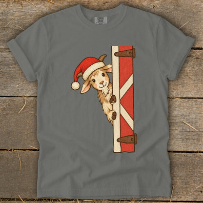 Goat in a Santa hat peeking from behind a red barn door graphic on a gray t-shirt.