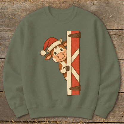 Green sweatshirt with a cartoon cow wearing a Santa hat peeking from behind a red barn door.