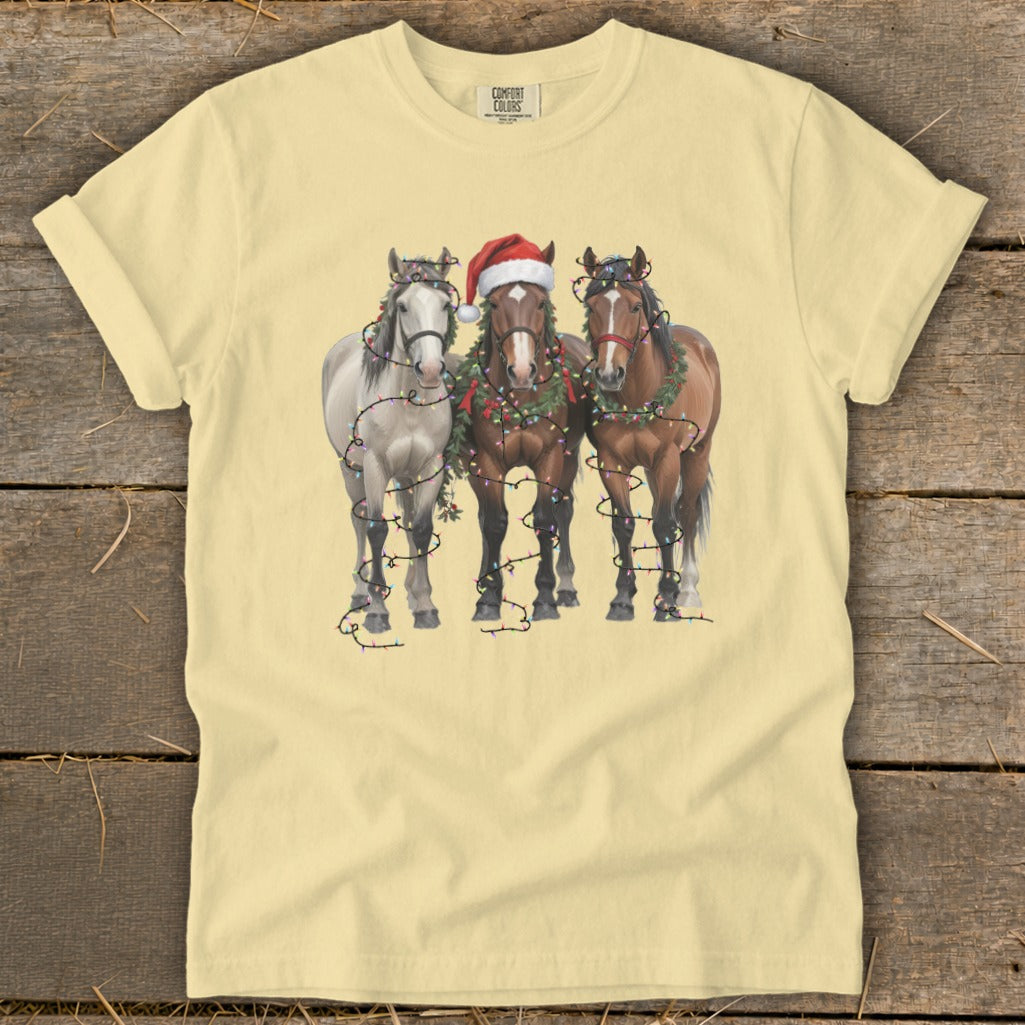 Three horses decorated with Christmas lights and wreaths, one wearing a Santa hat.