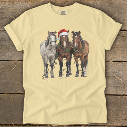 Three horses decorated with Christmas lights and wreaths, one wearing a Santa hat.