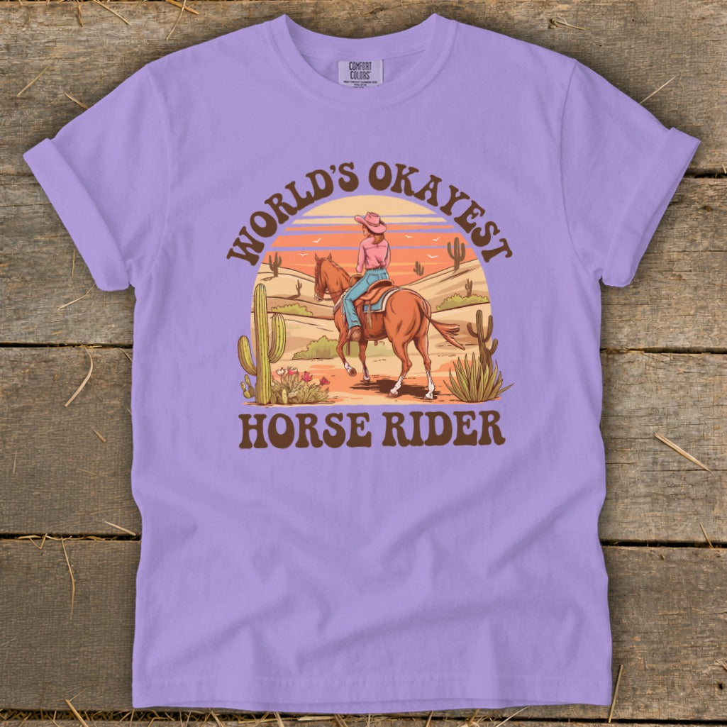 Purple t-shirt graphic with a cowboy and horse in a desert landscape and text.