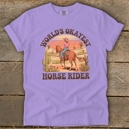 Purple t-shirt graphic with a cowboy and horse in a desert landscape and text.