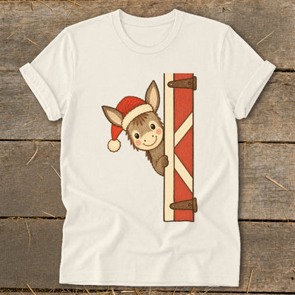 Donkey wearing Santa hat peeking around a barn door on a cream t-shirt.