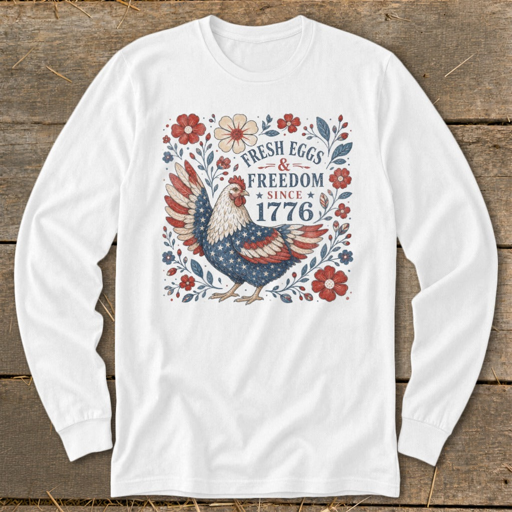 White long-sleeve shirt with a chicken and floral design reading "Fresh Eggs & Freedom Since 1776."