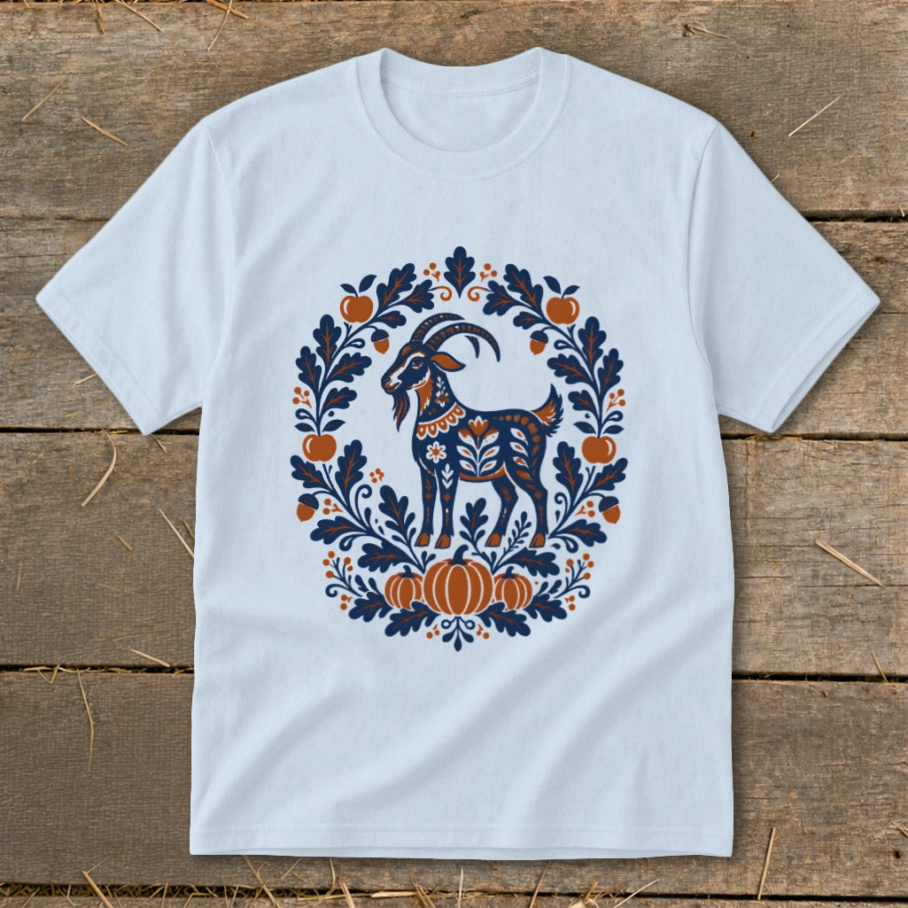 A light blue t-shirt with a folk-art graphic of a goat surrounded by autumn leaves and pumpkins.