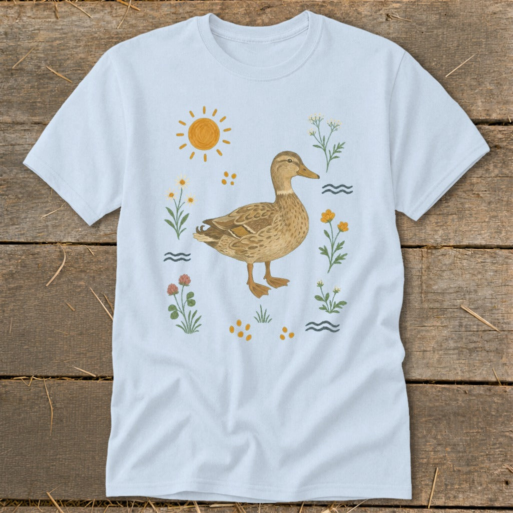 Light blue t-shirt with a watercolor illustration of a duck surrounded by flowers and sun.