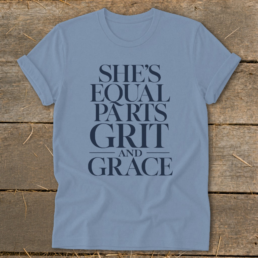 Light blue t-shirt with navy text "SHE'S EQUAL PARTS GRIT AND GRACE".