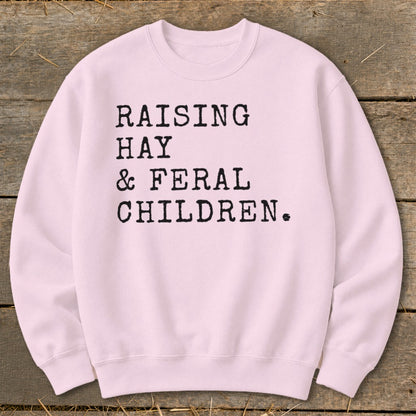 Pink sweatshirt with black text: "RAISING HAY & FERAL CHILDREN."
