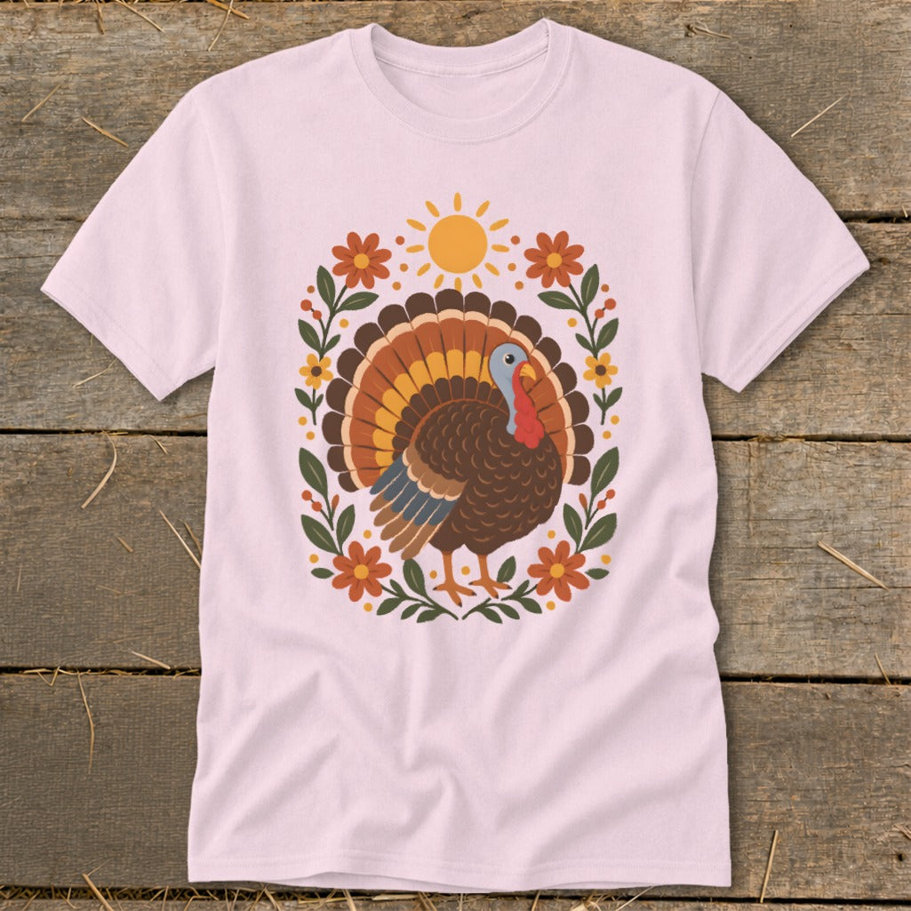 Pink t-shirt with a Thanksgiving turkey graphic surrounded by flowers and a sun.
