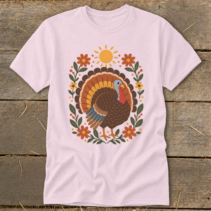 Pink t-shirt with a Thanksgiving turkey graphic surrounded by flowers and a sun.