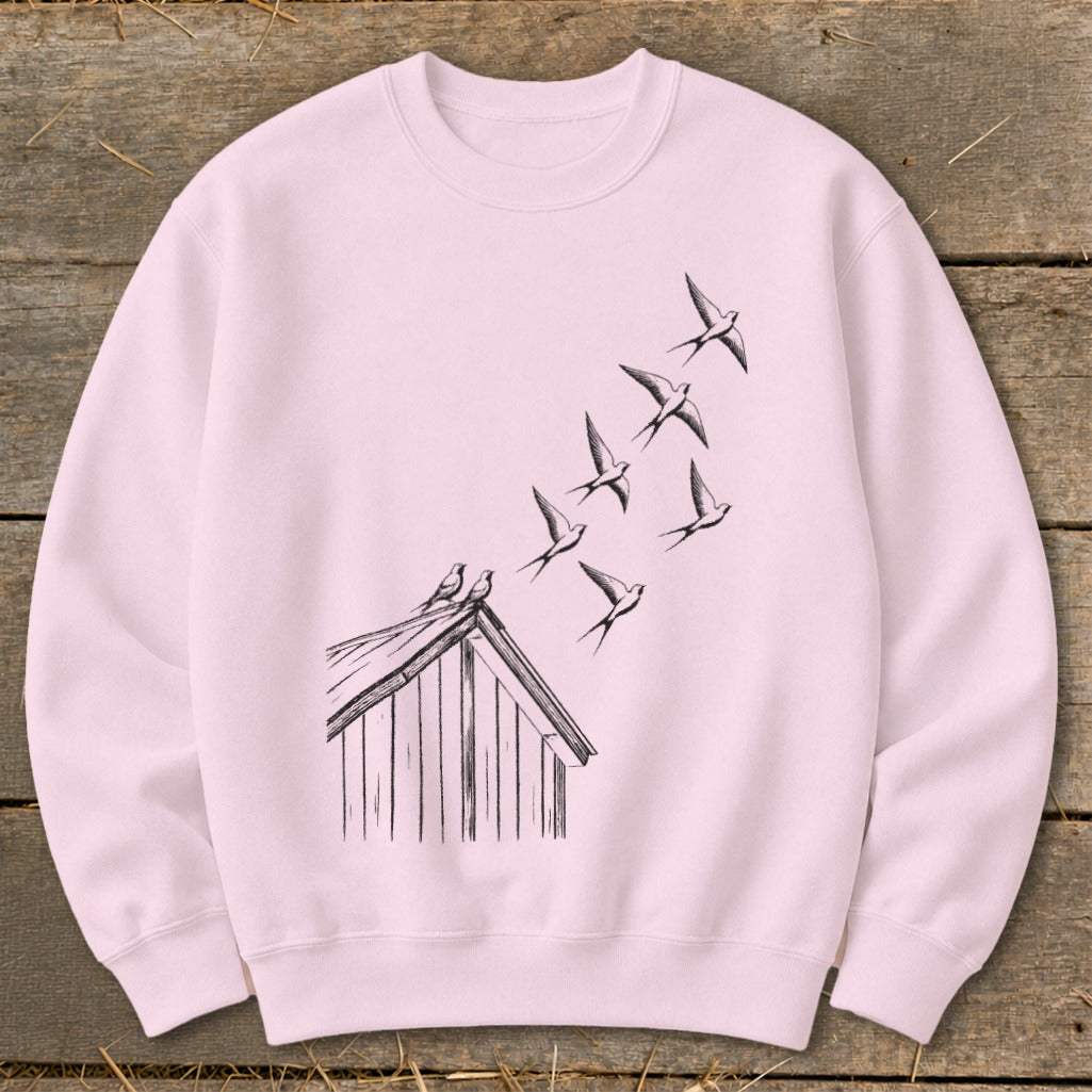 A light pink crewneck sweatshirt featuring a black sketch graphic of birds flying from a rooftop.