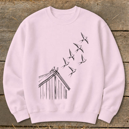 A light pink crewneck sweatshirt featuring a black sketch graphic of birds flying from a rooftop.