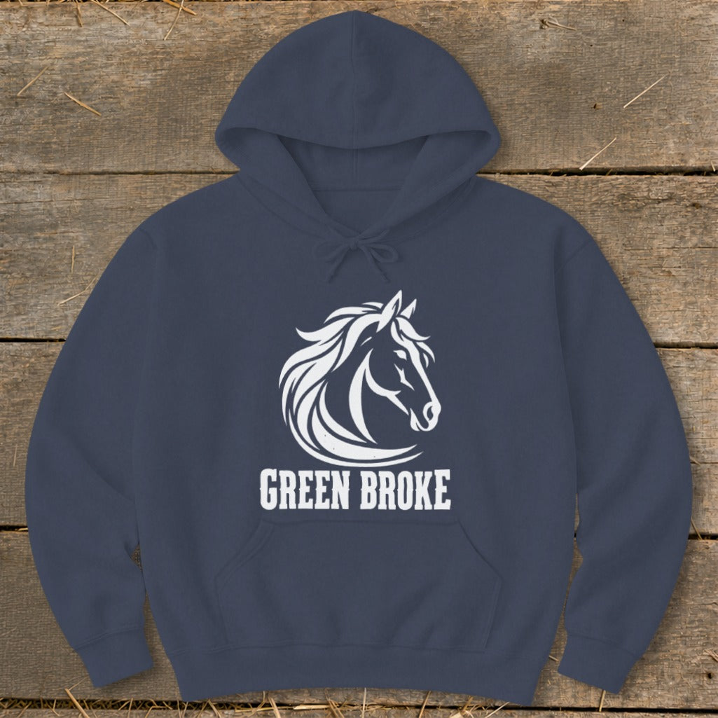 Navy blue hooded sweatshirt featuring a white graphic of a horse head and the text Green Broke laid on a rustic wooden background.