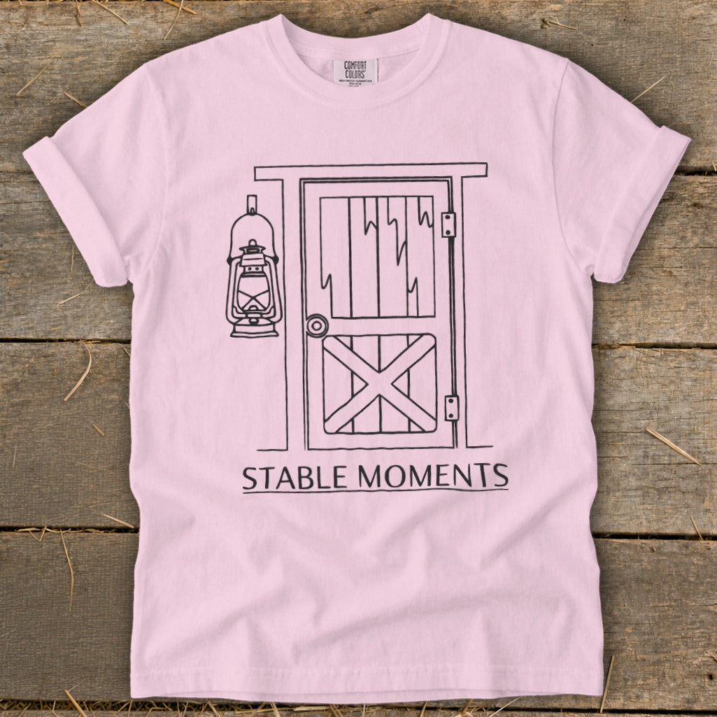 Pink t-shirt with a black line drawing of a barn door and lantern, reading "STABLE MOMENTS".