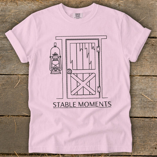 Pink t-shirt with a black line drawing of a barn door and lantern, reading "STABLE MOMENTS".