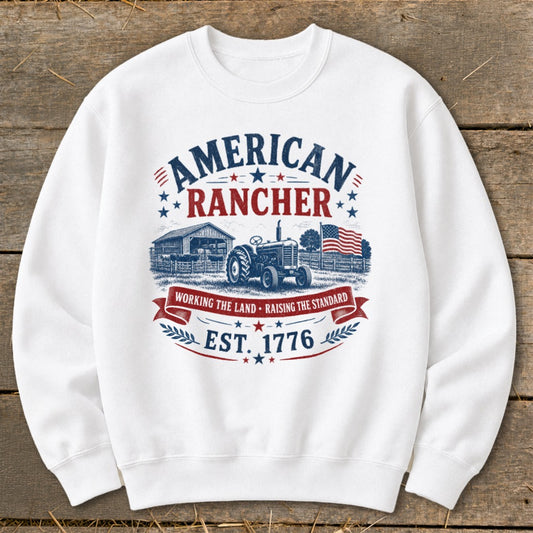 White sweatshirt with "American Rancher" graphic, tractor, barn, and American flag.
