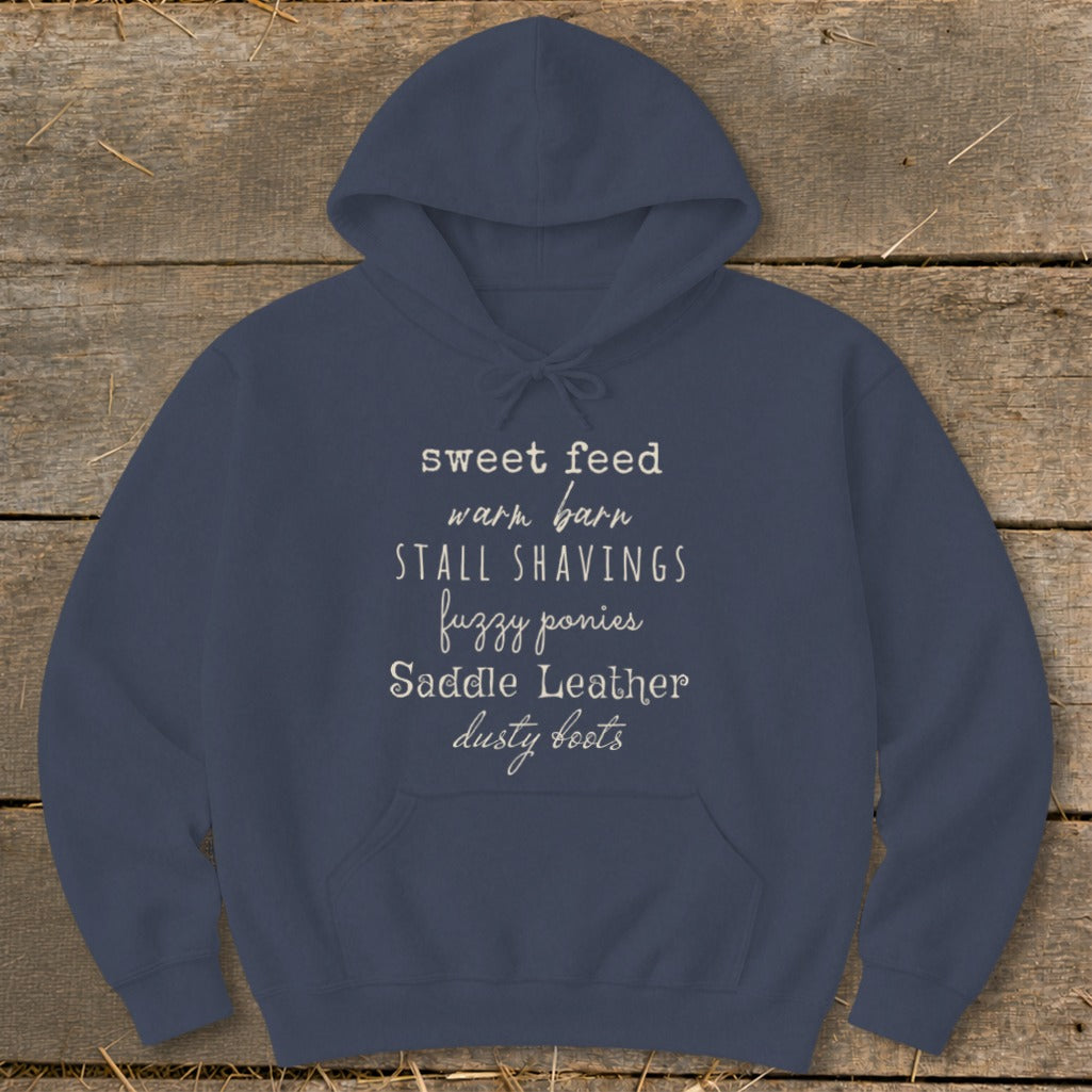 Navy hoodie with white text listing equestrian terms: sweet feed, warm barn, stall shavings, fuzzy ponies, saddle leather, dusty boots.