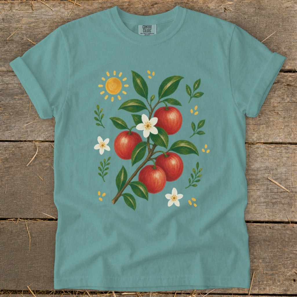 Teal t-shirt with illustration of red apples on a branch, white blossoms, and sun.
