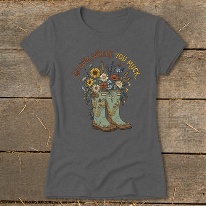 Grey t-shirt with green boots overflowing with flowers and the text "Bloom Where You Muck".