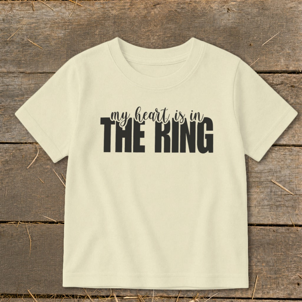 Cream t-shirt with black text "my heart is in THE RING" on a wooden background.