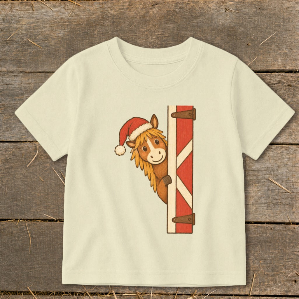 Cream t-shirt with cartoon horse wearing Santa hat peeking from barn door.