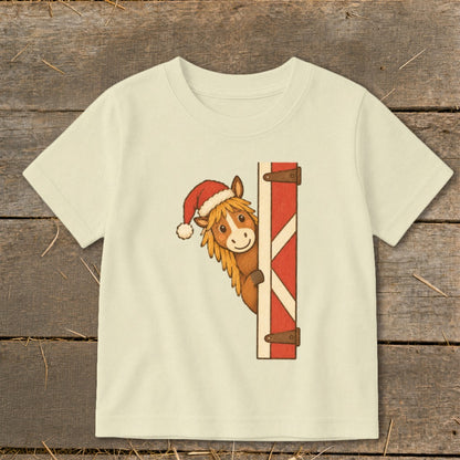 Cream t-shirt with cartoon horse wearing Santa hat peeking from barn door.