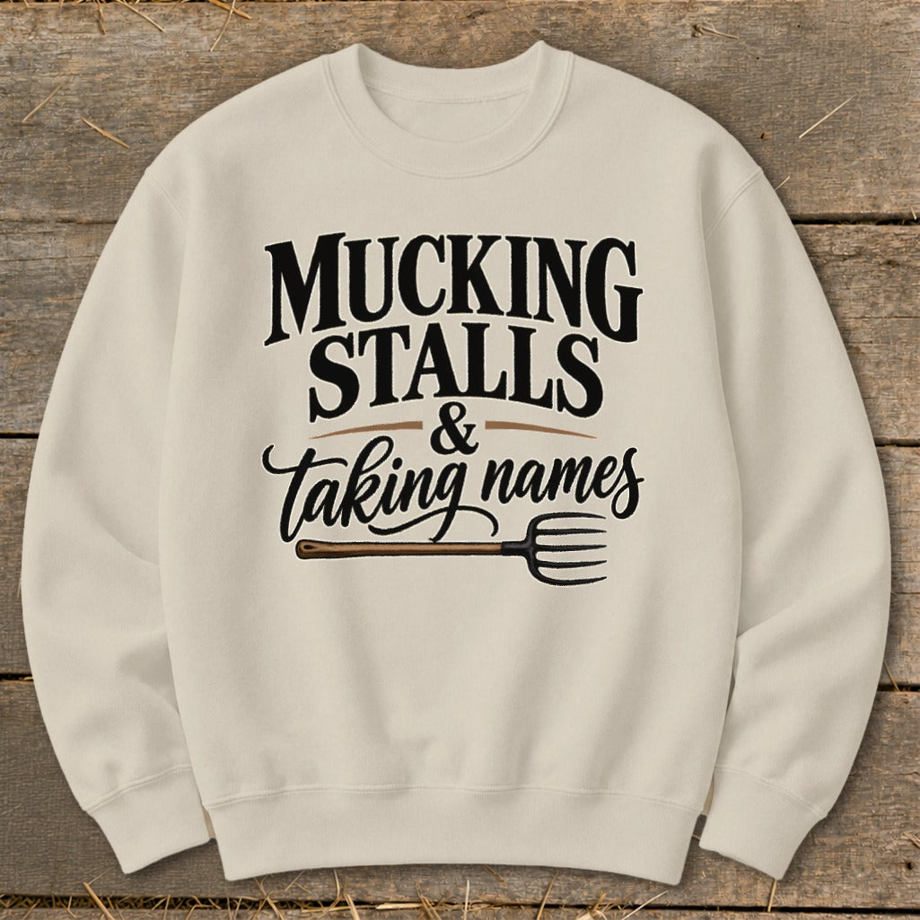 Cream sweatshirt with "MUCKING STALLS & taking names" text and a pitchfork graphic.