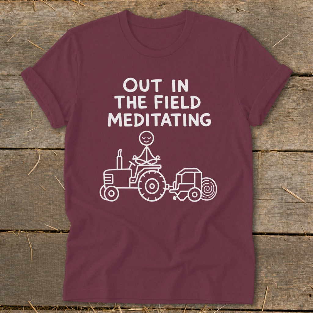 Maroon t-shirt with "Out in the Field Meditating" text and a stick figure on a tractor.