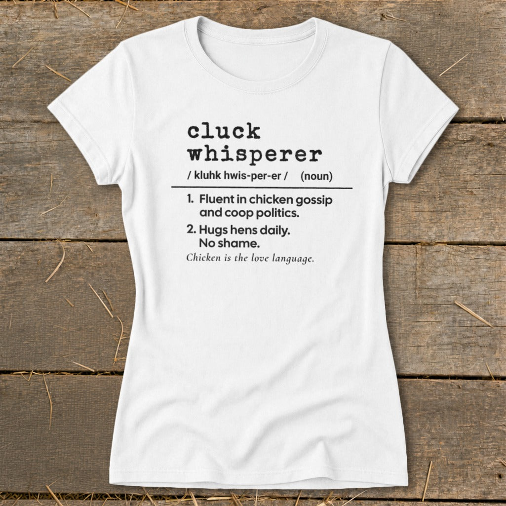 White t-shirt with black text defining "cluck whisperer" as fluent in chicken gossip and hugs hens.