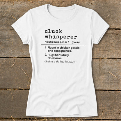 White t-shirt with black text defining "cluck whisperer" as fluent in chicken gossip and hugs hens.