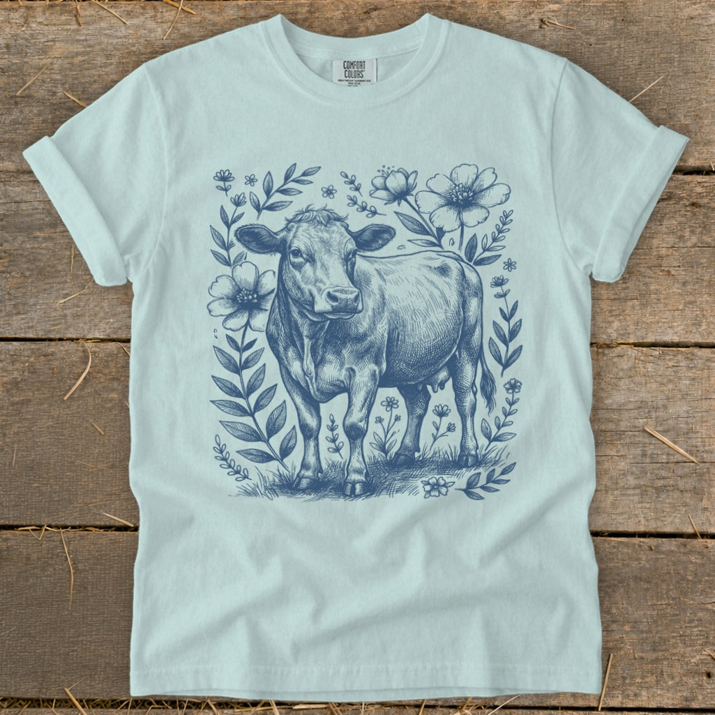 Light blue t-shirt with a blue sketch of a cow surrounded by floral elements.