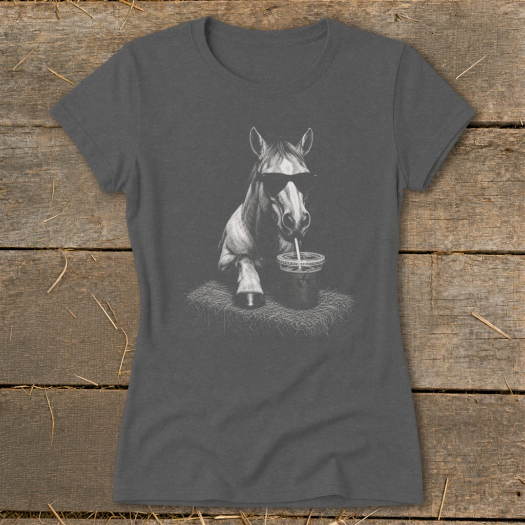 Horse wearing sunglasses drinks from cup with straw on a hay bale.