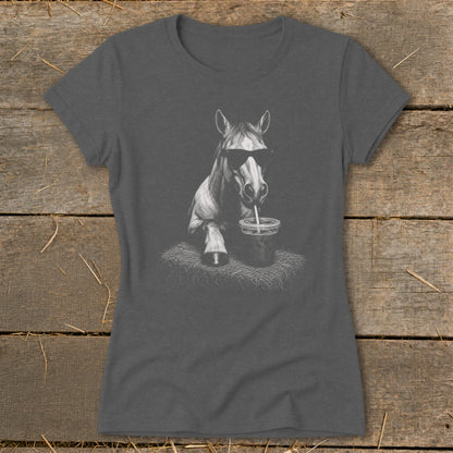 Horse wearing sunglasses drinks from cup with straw on a hay bale.