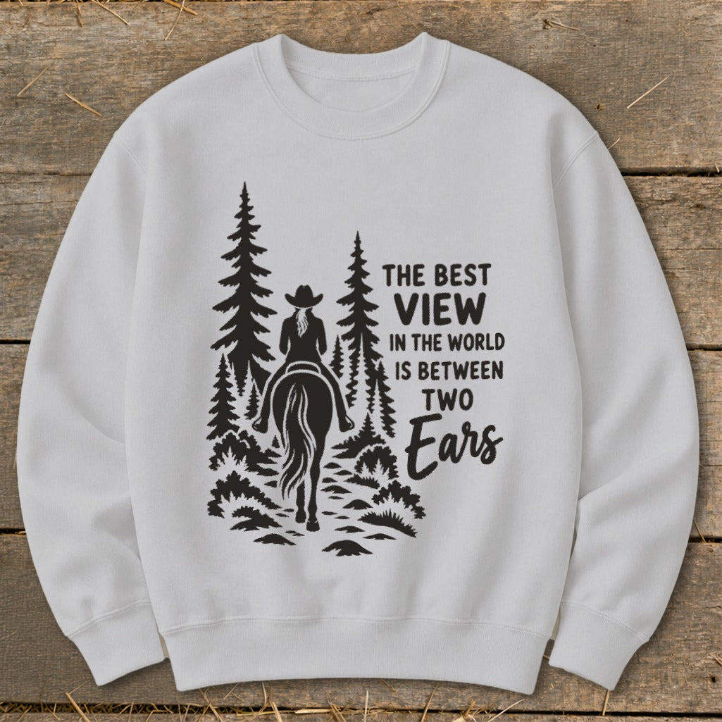 A light gray crewneck sweatshirt features a black graphic of a horse rider in the woods with text reading The Best View In The World Is Between Two Ears.