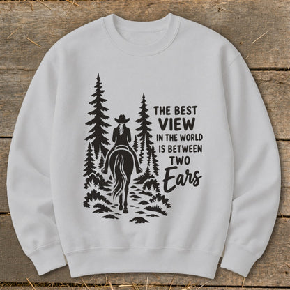 A light gray crewneck sweatshirt features a black graphic of a horse rider in the woods with text reading The Best View In The World Is Between Two Ears.