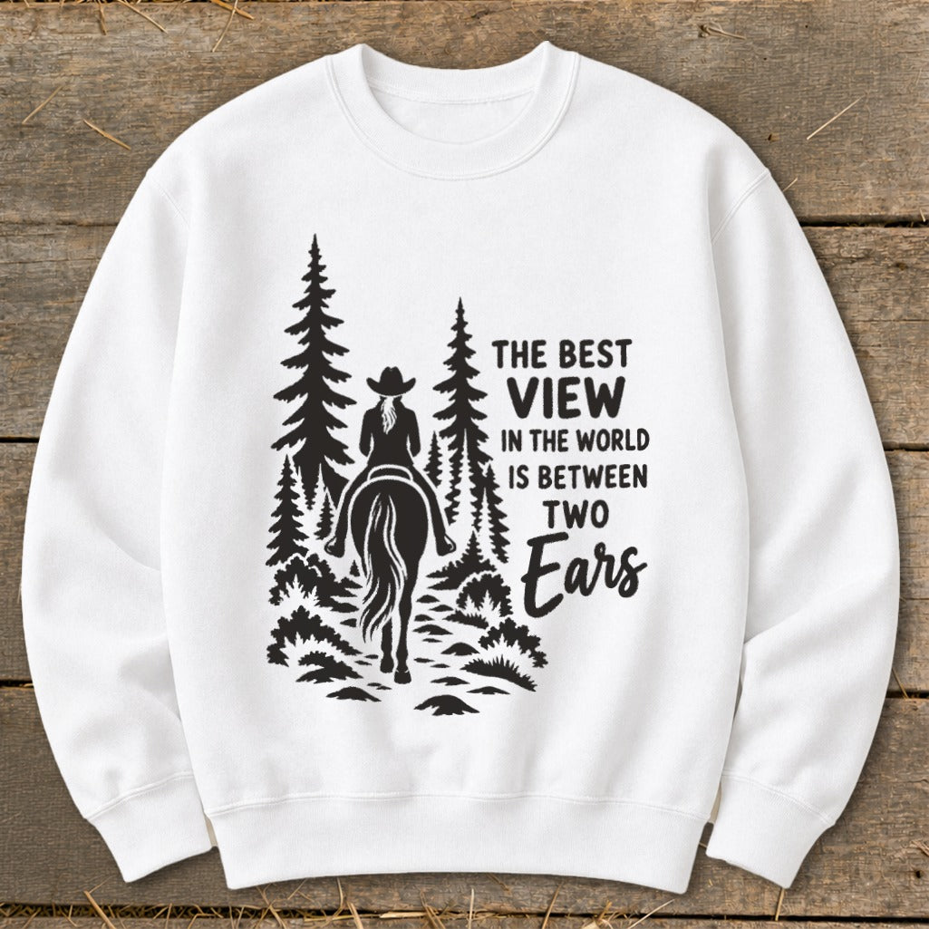 A white crewneck sweatshirt featuring a black graphic of a horseback rider in a forest with the text, The Best View in the World is Between Two Ears.