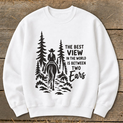 A white crewneck sweatshirt featuring a black graphic of a horseback rider in a forest with the text, The Best View in the World is Between Two Ears.
