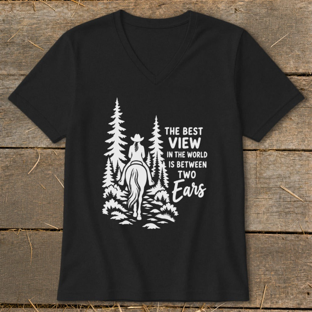 A black V-neck t-shirt displays a white graphic of a horseback rider amidst pine trees, accompanied by the text "THE BEST VIEW IN THE WORLD IS BETWEEN TWO EARS".