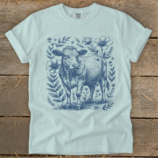 Light blue t-shirt with a blue sketch of a cow surrounded by floral elements.