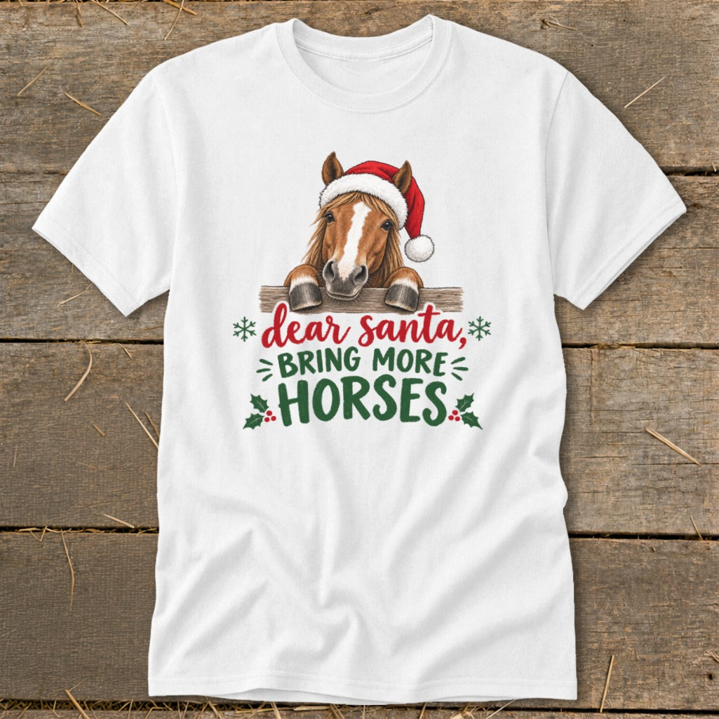 A white short-sleeved t-shirt featuring a horse wearing a Santa hat behind a fence with text that reads dear santa, bring more horses.