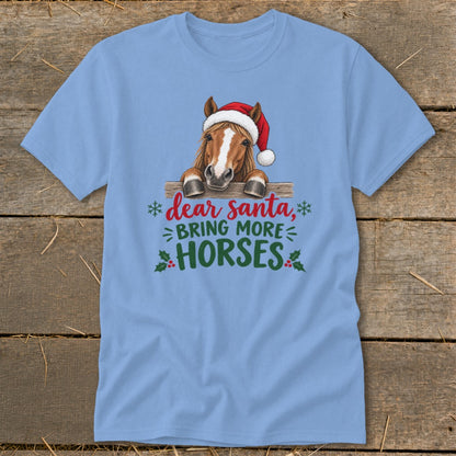 A light blue t-shirt featuring a horse wearing a Santa hat behind a wooden fence with text saying, "Dear Santa, Bring More Horses."
