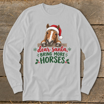 A light gray long-sleeve t-shirt featuring a horse wearing a Santa hat behind a fence, with the text "dear santa, BRING MORE HORSES."