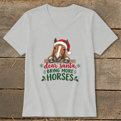A light gray V-neck T-shirt featuring a graphic of a horse wearing a Santa hat behind a fence with the text "dear santa, bring more horses".