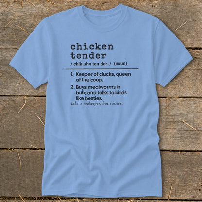 A light blue t-shirt printed with a humorous definition of a chicken tender resting on a wooden surface.