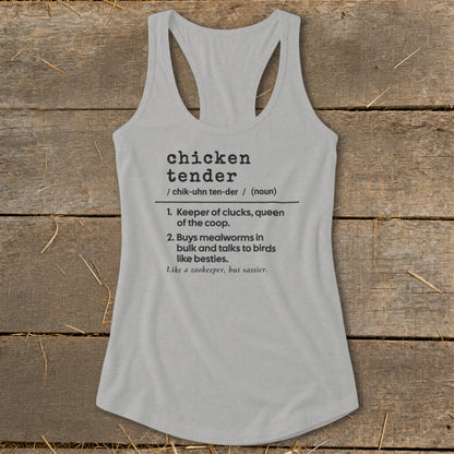 A grey women's racerback tank top printed with a humorous definition of chicken tender resting on a rustic wooden background.