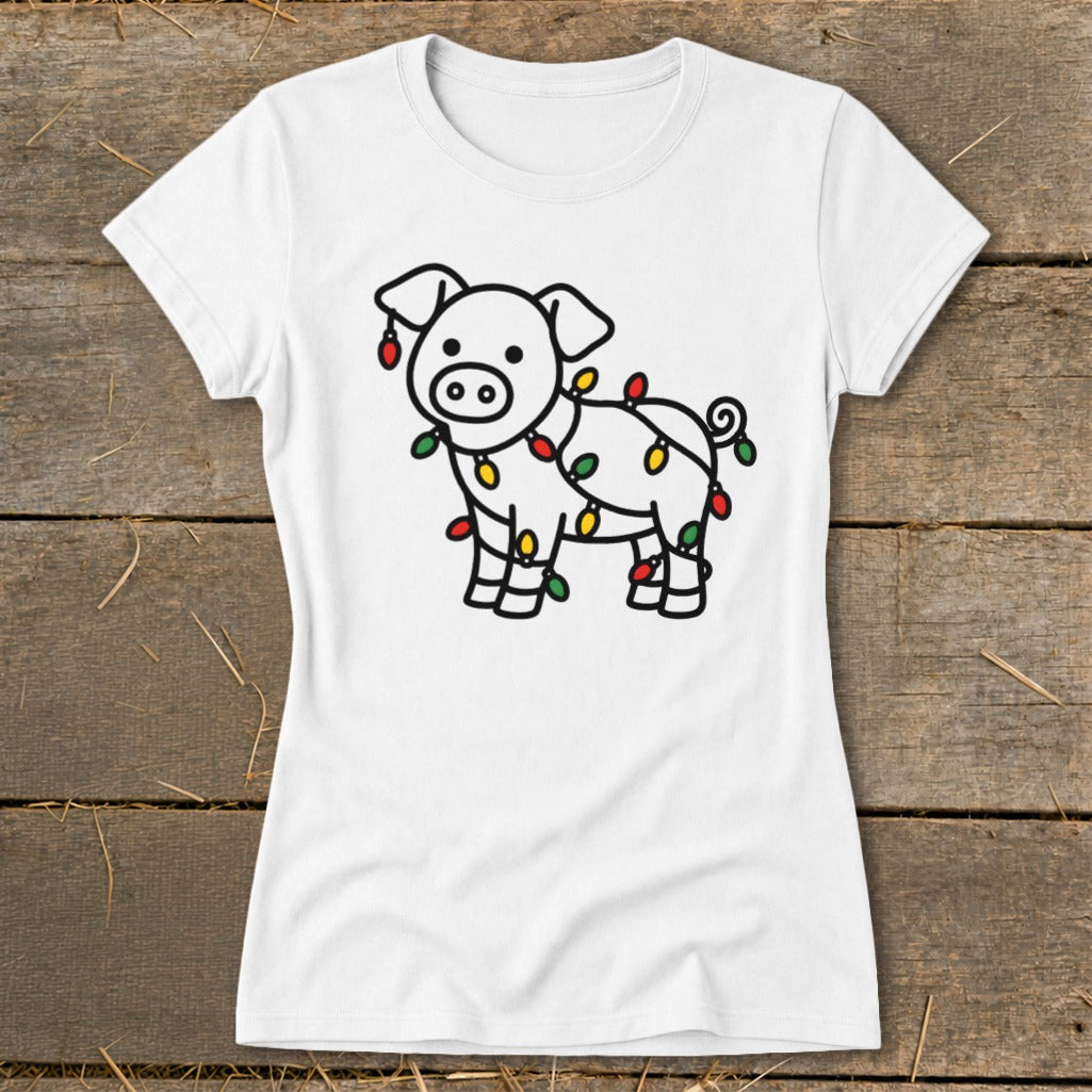 A white t-shirt featuring a cartoon pig wrapped in colorful Christmas lights, displayed on a wooden surface.