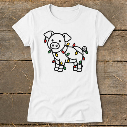 A white t-shirt featuring a cartoon pig wrapped in colorful Christmas lights, displayed on a wooden surface.