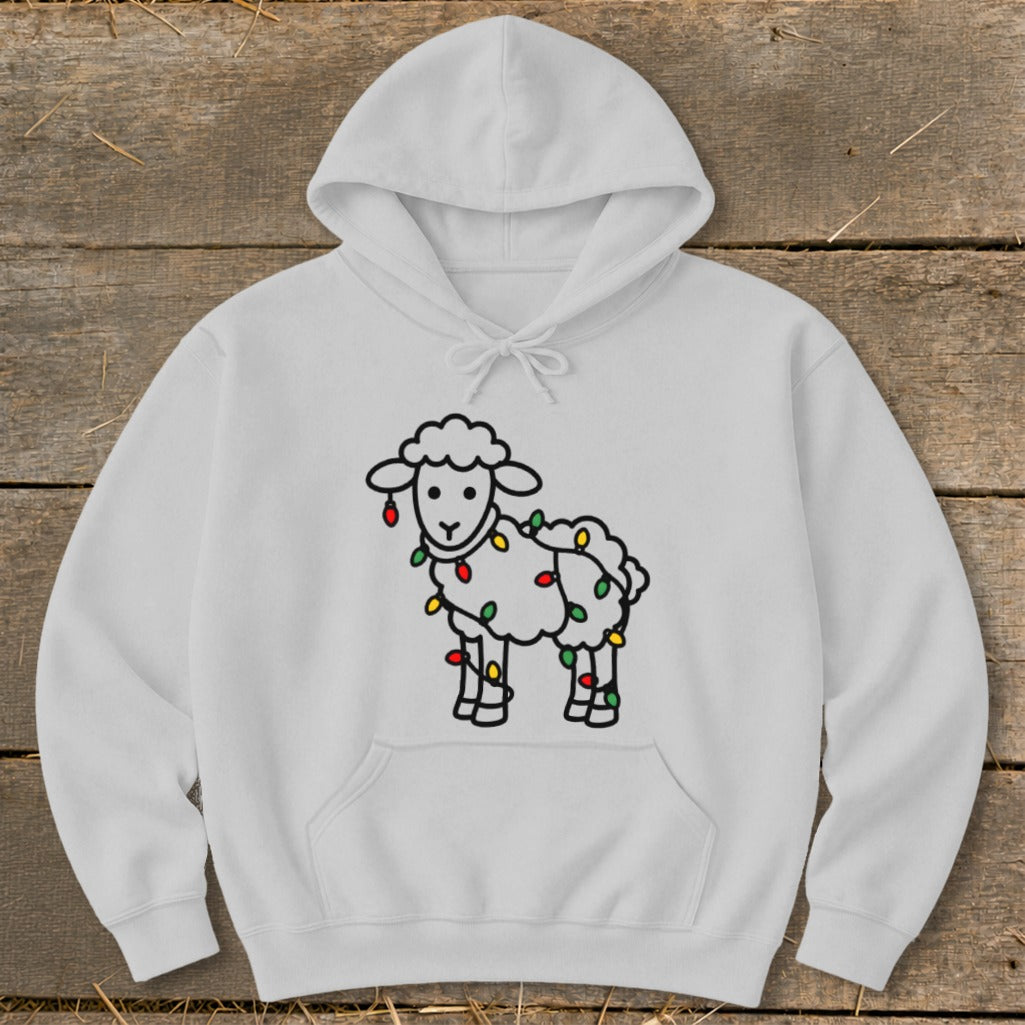 A light gray hooded sweatshirt featuring a cartoon sheep wrapped in colorful Christmas lights, laid flat on a wooden background.